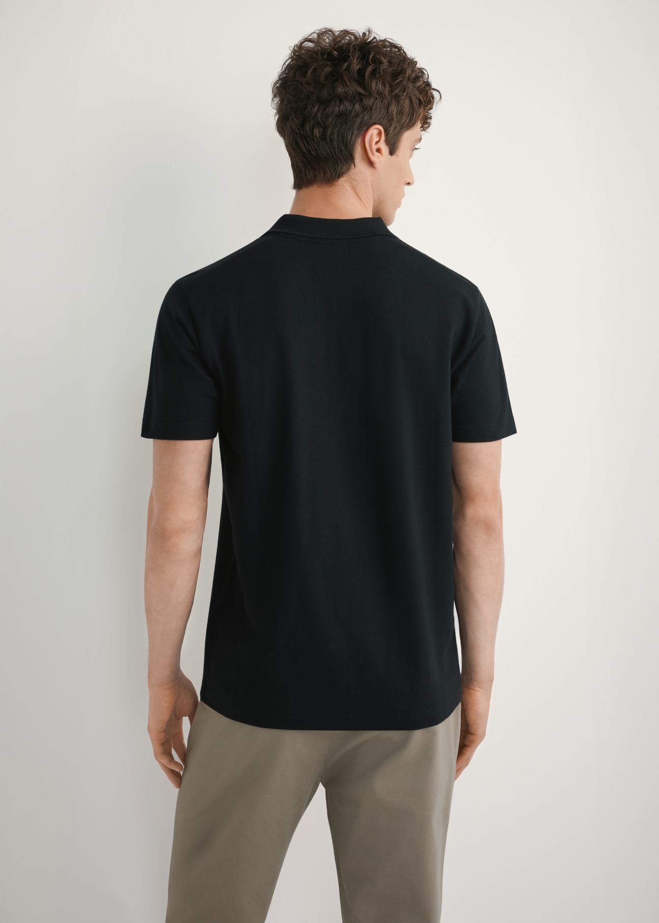 Czarna koszulka polo męska POLMT-0084-99(W26) - widok produktu z tyłu, na modelu, na jasnym tle. Widoczna połowa sylwetki. 