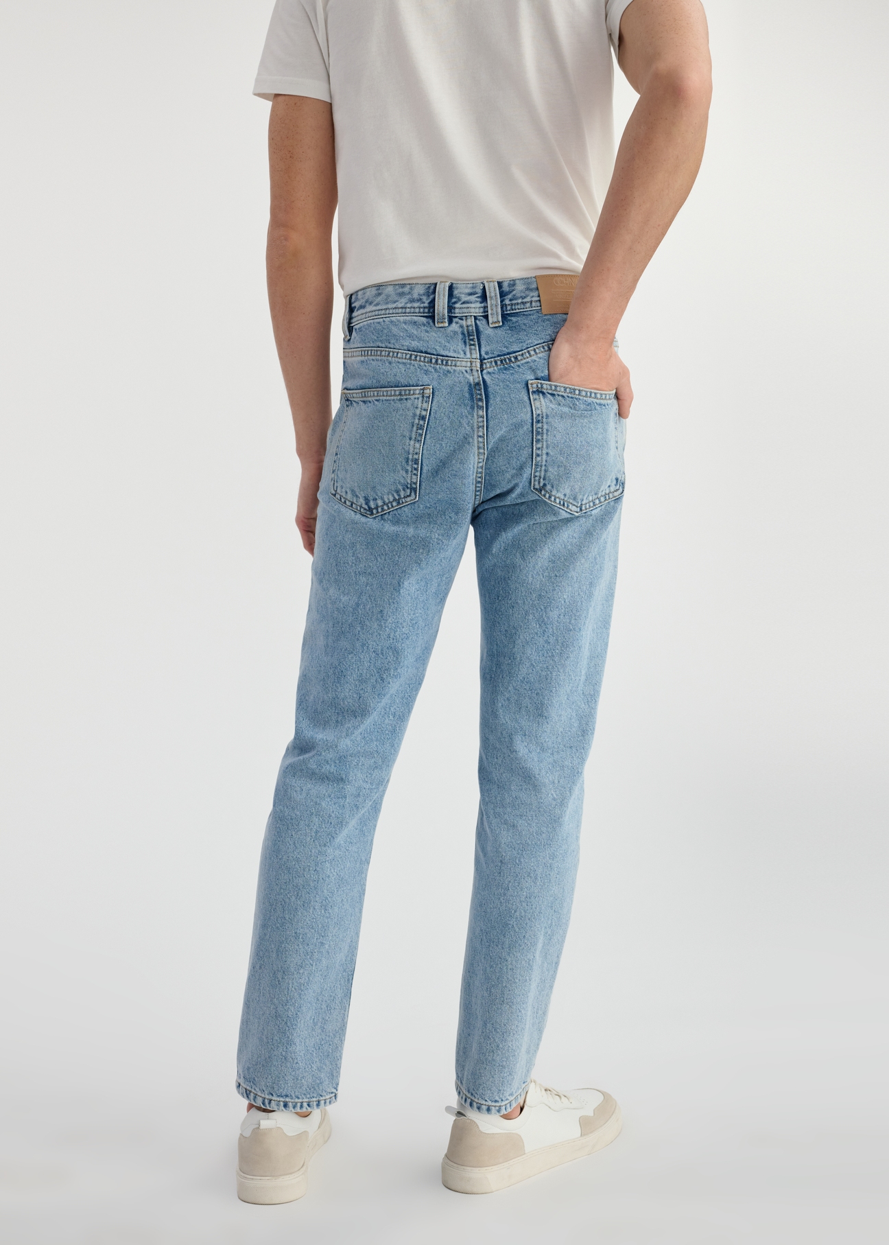 Niebieskie spodnie jeansowe męskie JEAMT-0024-60(W25) - widok produktu z tyłu na modelu na białym tle. Widoczna połowa sylwetki.