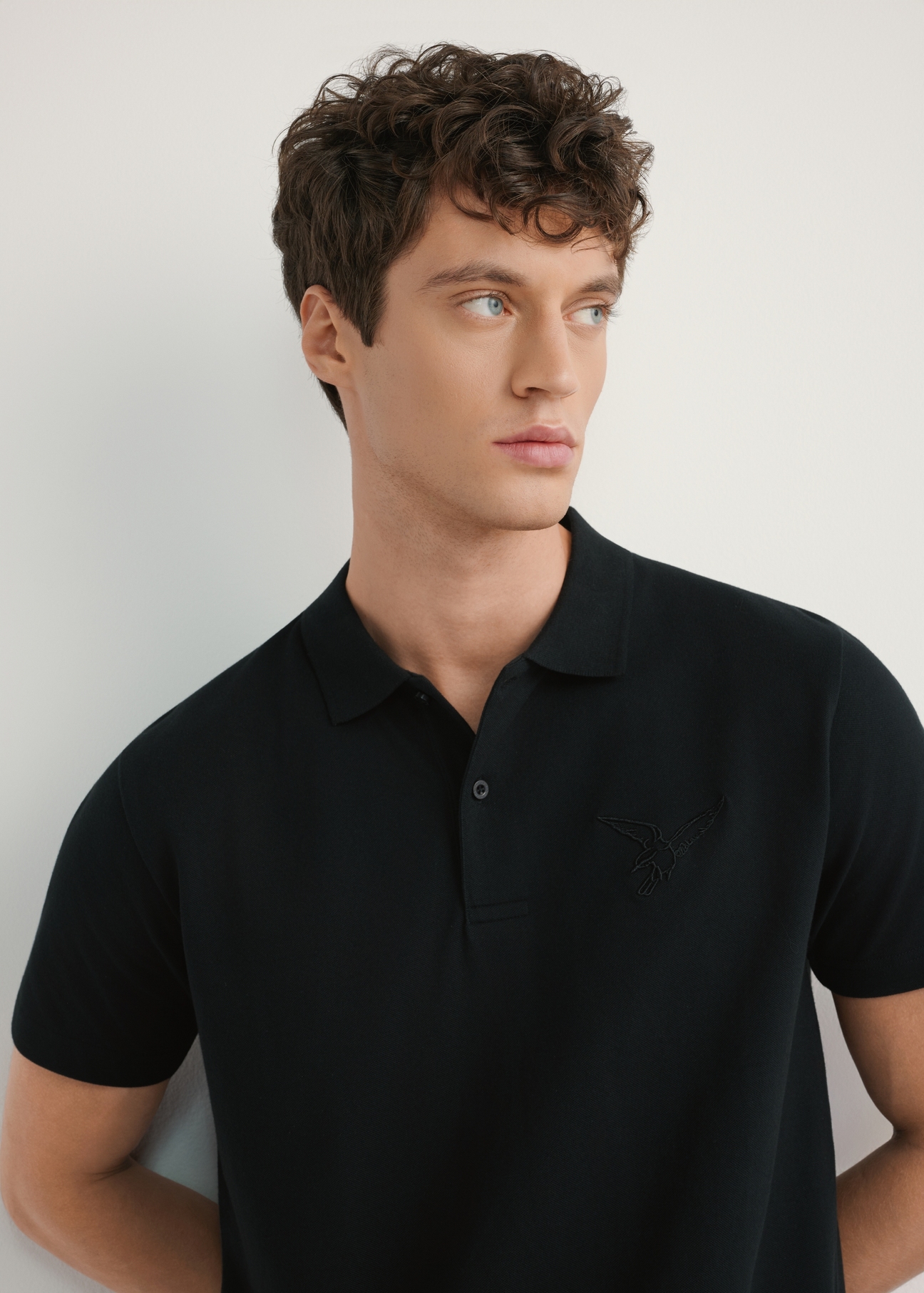 Czarna koszulka polo męska POLMT-0084-99(W26) - widok produktu z przodu, na modelu, na jasnym tle. Widoczna połowa sylwetki. 