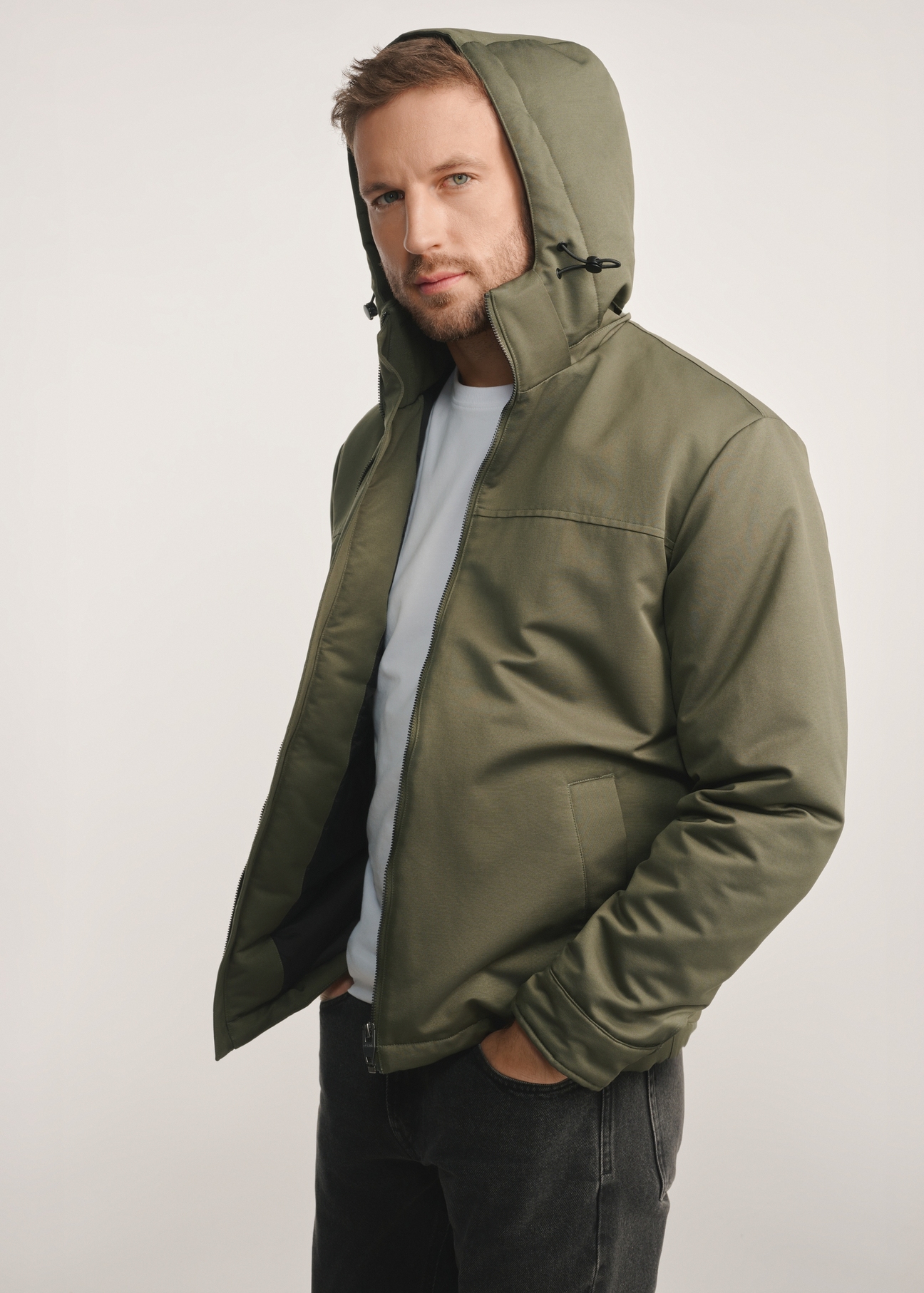Kurtka męska w kolorze khaki KURMT-0386-54(Z25) - widok produktu z boku na modelu na białym tle. Widoczna sylwetka do kolan. 