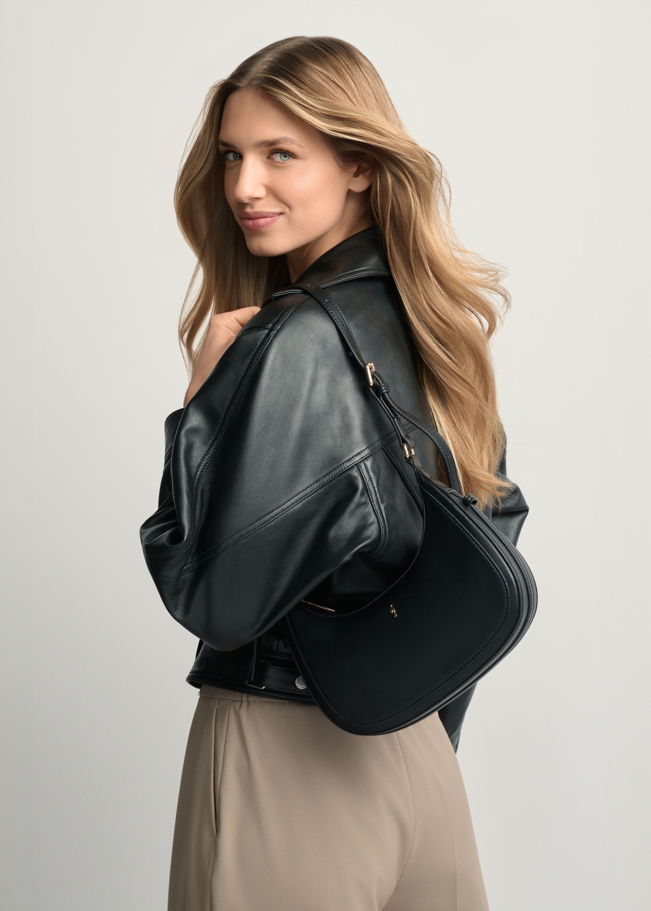 Czarna mała torebka hobo TOREC-1136-99(W26) - widok produktu z po skosie, na modelce stojącej tyłem, na jasnym tle. Widoczna połowa sylwetki. 
