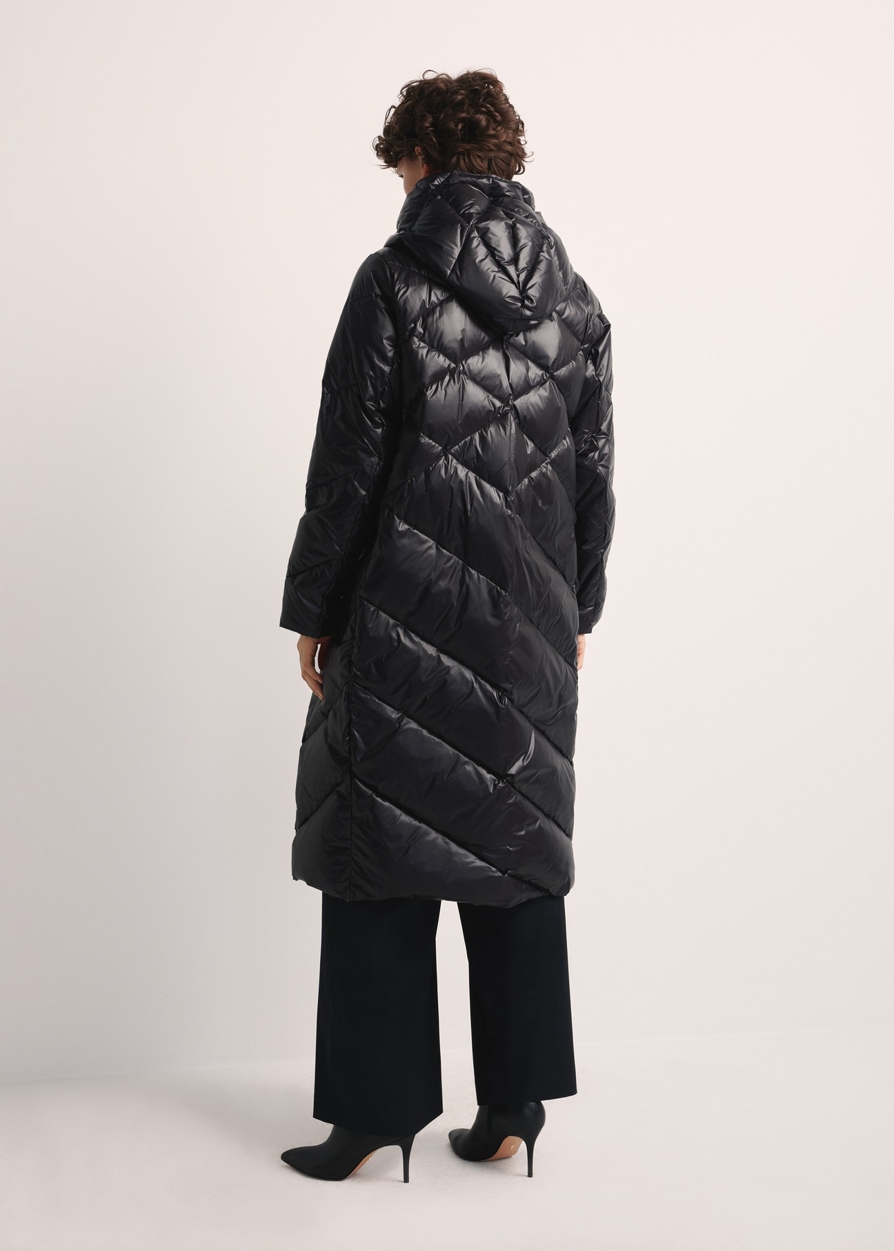 Długa czarna kurtka zimowa damska KURDT-0542A-98(Z25), widok produktu z tyłu na modelce, widoczna cała sylwetka.