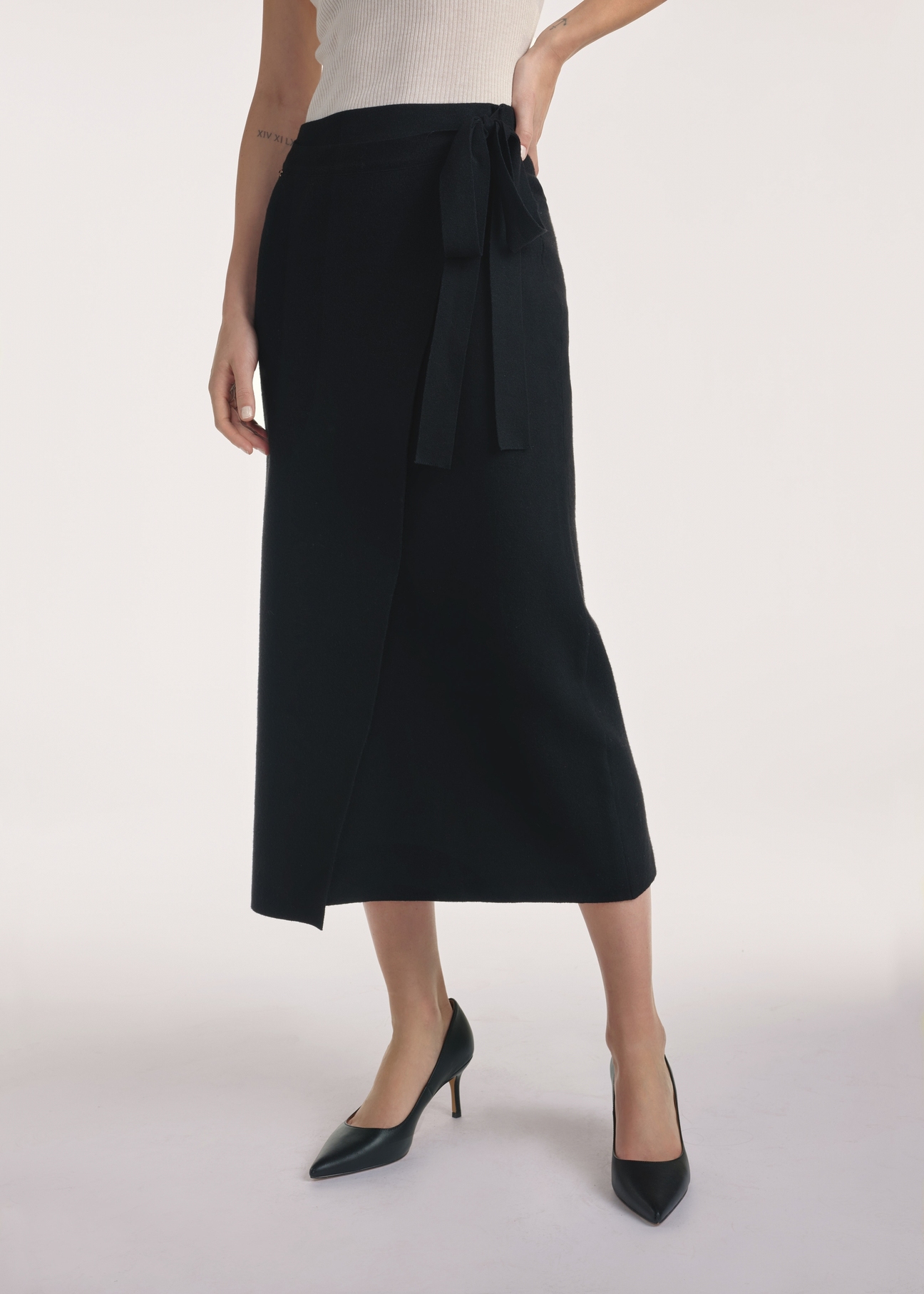 Czarna spódnica midi SPCDT-0114-99(Z25), widok produktu z przodu na modelce, widoczne pół sylwetki.