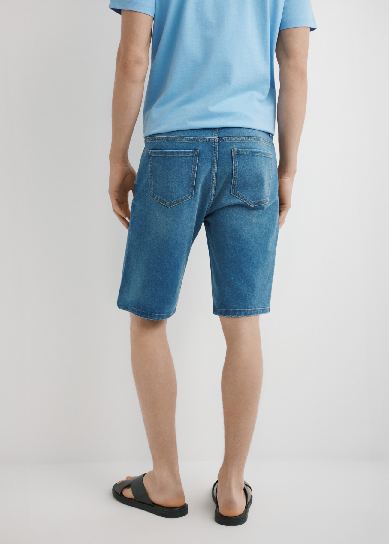 Niebieskie jeansowe szorty męskie SZOMT-0036-7H(W26) - widok produktu z tyłu na modelu, na jasnym tle. Widodczna połowa sylwetki.
