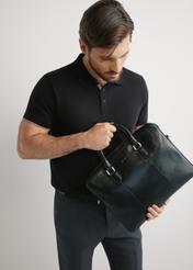 Czarna skórzana męska torba na laptopa TORMS-0506-99(W26) - widok produktu, trzymanego przez modela w ręku, na jasnym tle. 