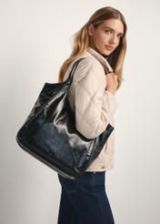 Czarna torebka damska shopper TOREC-1122-9F(W26) - widok produktu z przodu, na modelce stojącej bokiem, na jasnym tle. Widoczna połowa sylwetki. 
