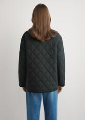 Czarna pikowana kurtka damska KURDT-0580-99(W26) - widok produktu z tyłu, na modelce, na jasnym tle. Widoczna sylwetka do kolan.
