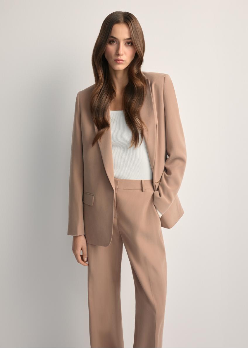 Marynarka damska w kolorze camelowym ZAKDT-0031A-1D(W26) - widok produktu z przodu, na modelce, na jasnym tle. Widoczna sylwetka do kolan. 